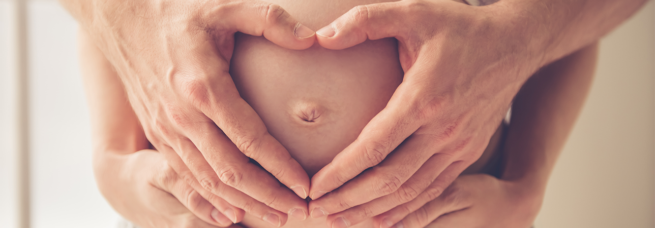 Pregnant woman gently holding her belly and smiling happily